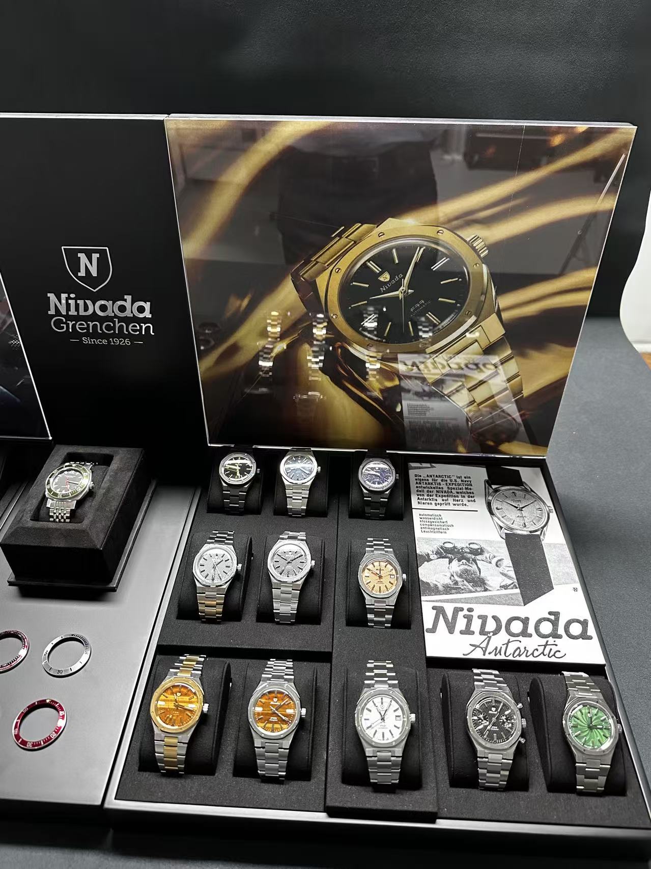 Collection of Nivada watches displayed in a box with promotional material.
