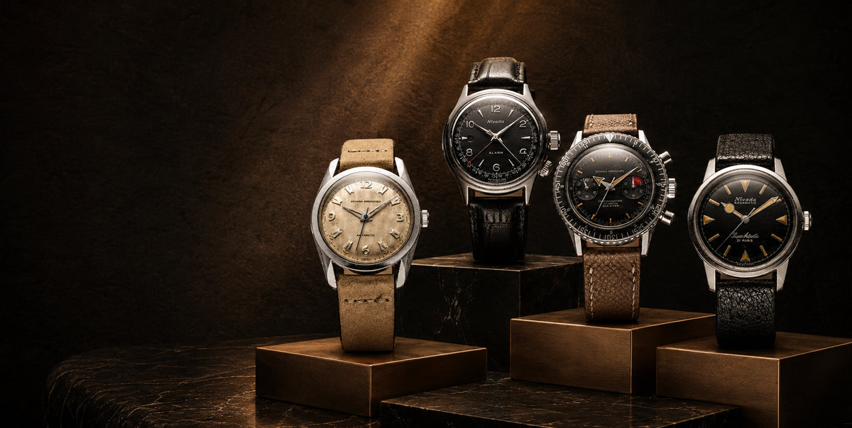 Four vintage Nivada Grenchen watches on bronze and dark marble pedestals under warm spotlight