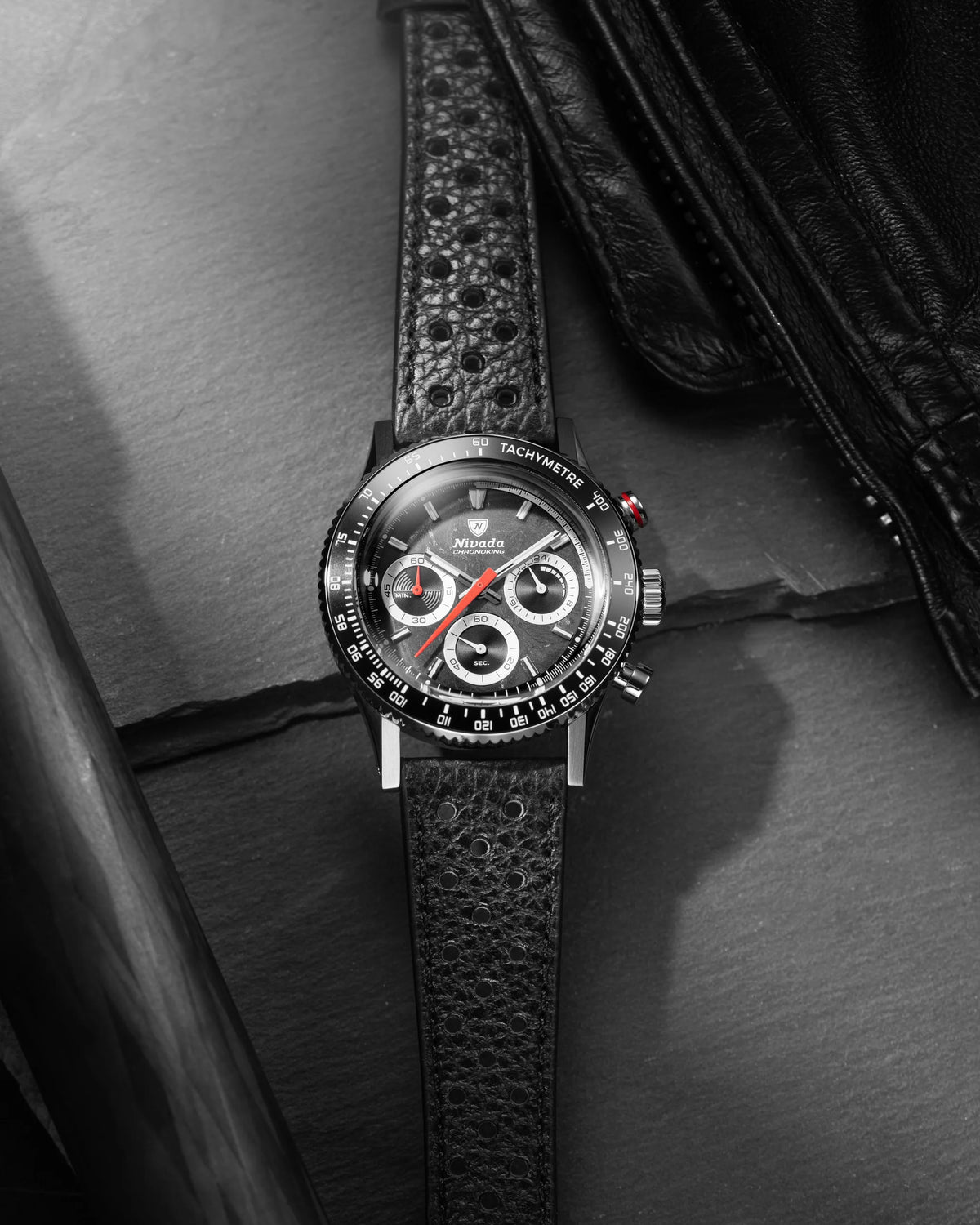 Nivada Grenchen Chronoking Mecaquartz Racing Black on perforated leather strap beside a black leather jacket