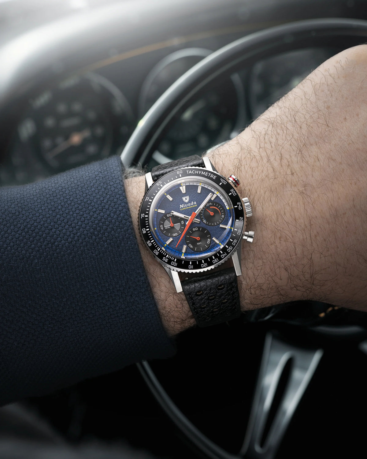Nivada Grenchen Chronoking Mecaquartz Racing Blue on a wrist resting on a car steering wheel