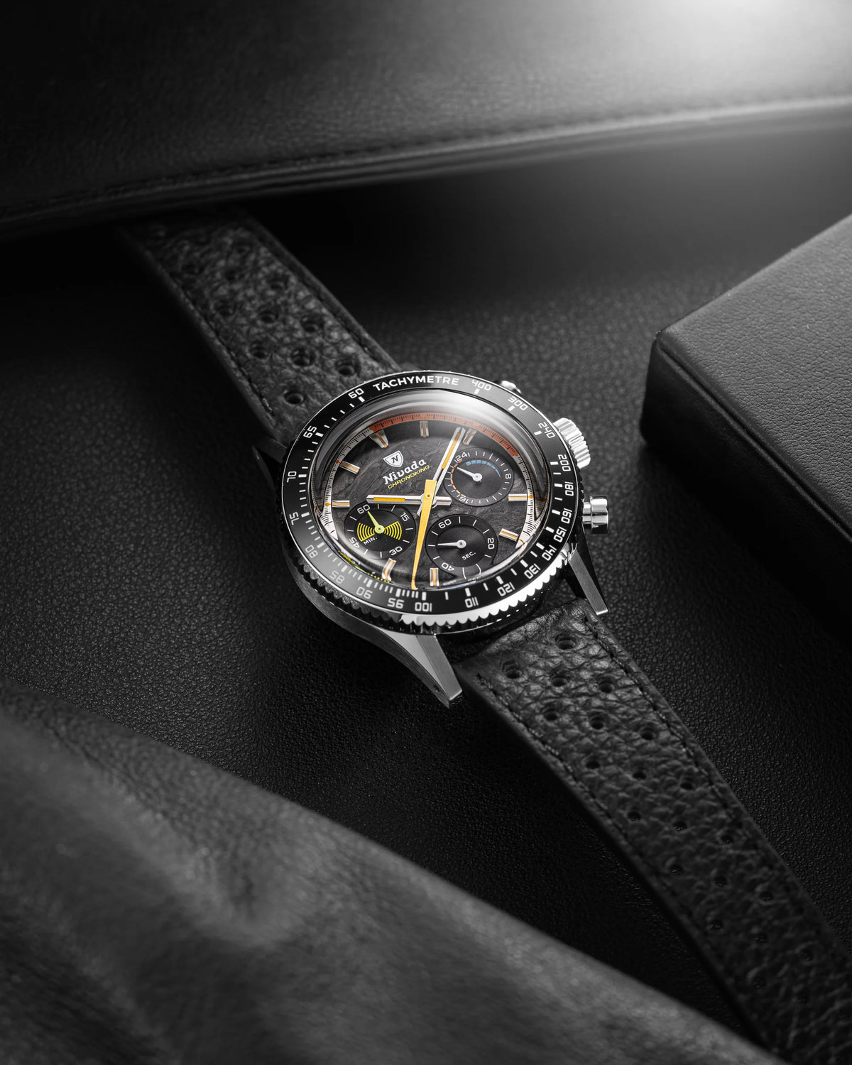 Nivada Grenchen Chronoking Mecaquartz Racing Carbon with black bezel and perforated leather strap on dark leather surface