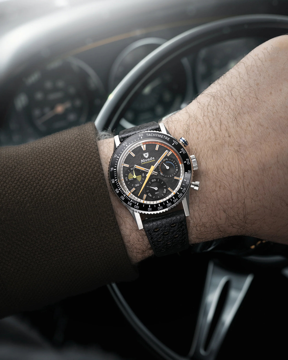 Nivada Grenchen Chronoking Mecaquartz Racing Carbon worn on wrist in front of a classic car steering wheel